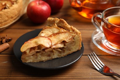 Photo of Slice of delicious apple pie served with tea on wooden table, closeup