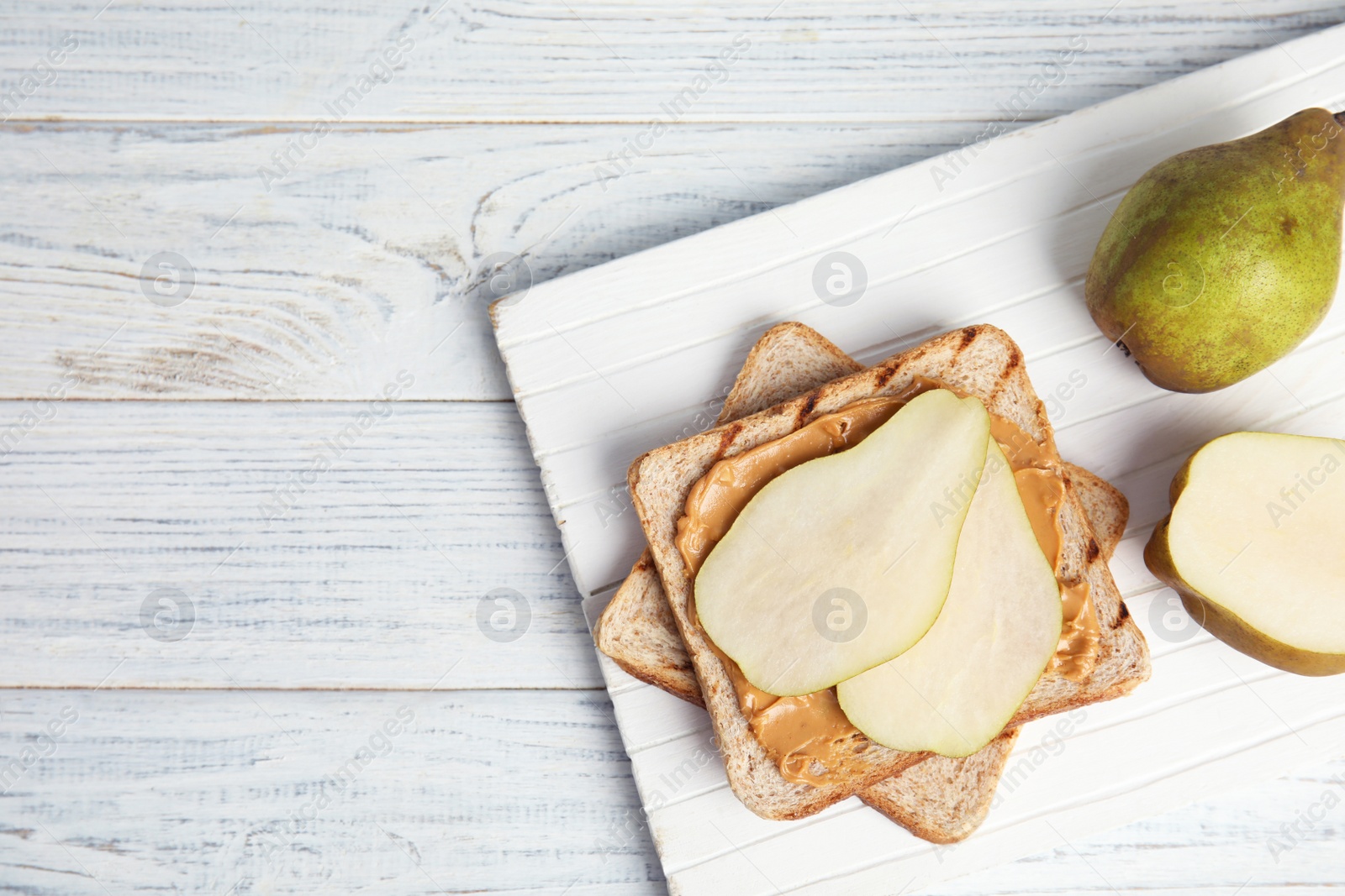 Photo of Slice of bread with peanut butter and pear on white wooden table, flat lay. Space for text