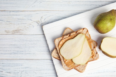 Slice of bread with peanut butter and pear on white wooden table, flat lay. Space for text