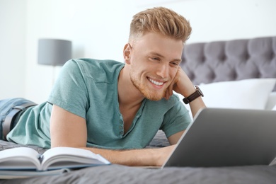 Photo of Young man using laptop while lying on bed at home