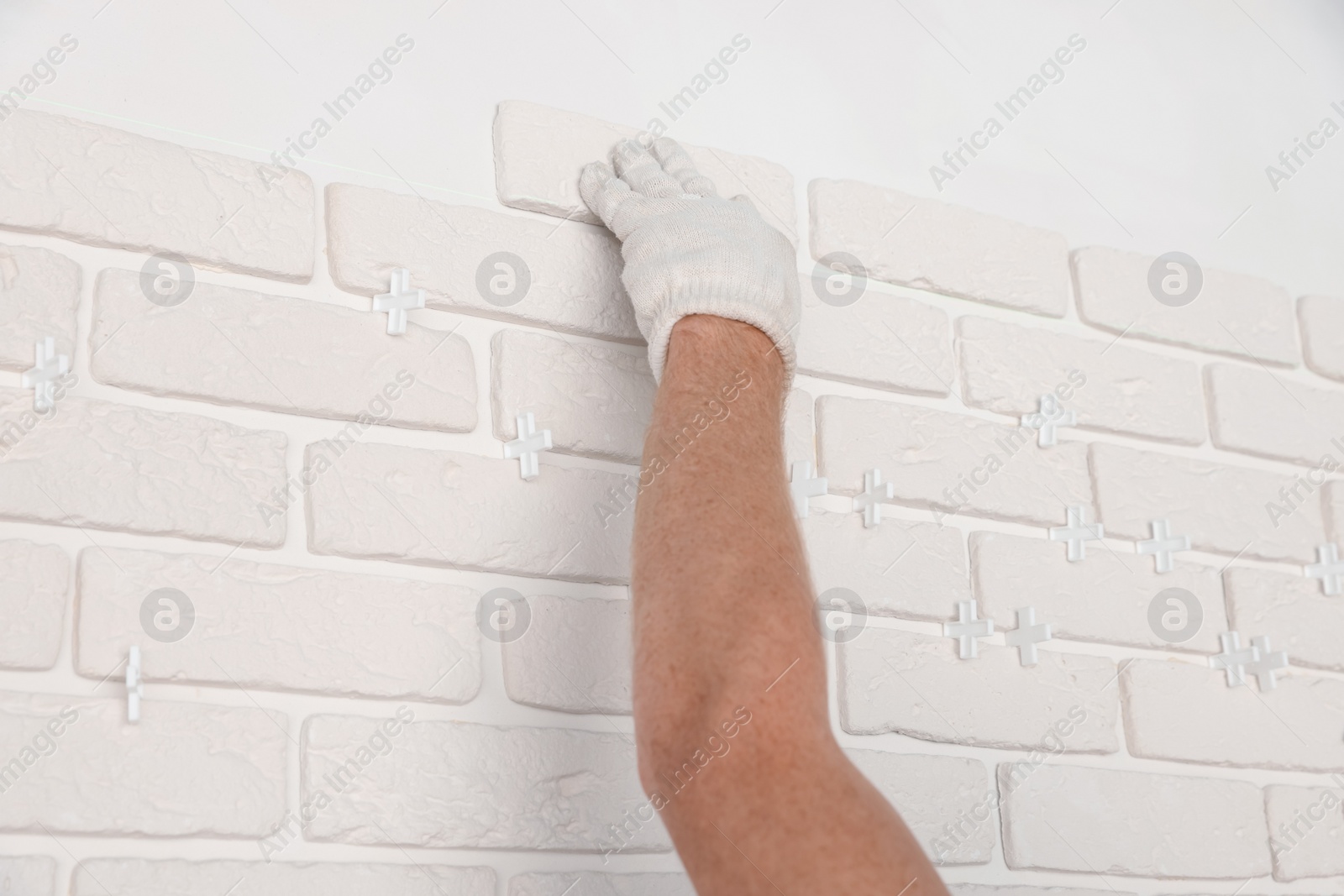 Photo of Professional builder installing new white decorative bricks on wall, closeup