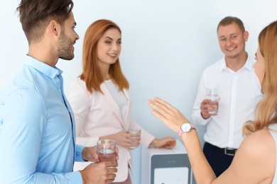 Photo of Co-workers having break near water cooler on white background
