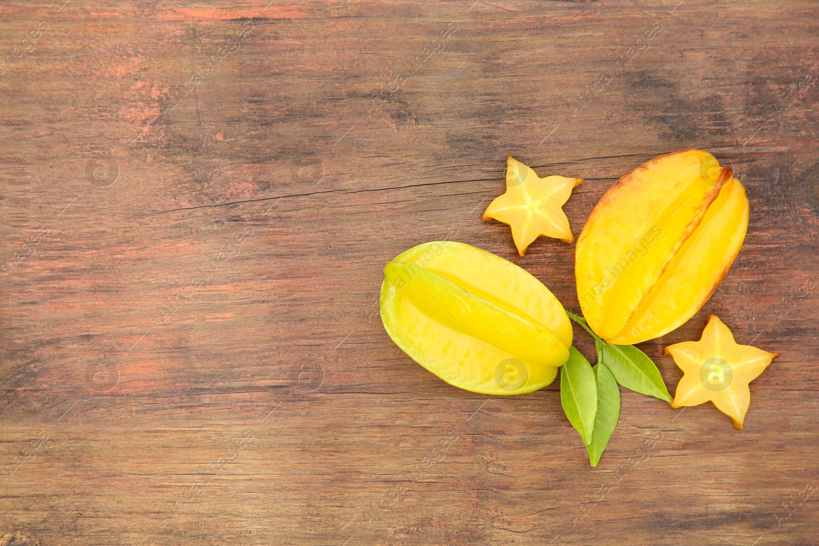 Photo of Cut and whole delicious ripe carambolas with leaves on wooden table, flat lay. Space for text