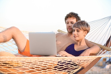 Young couple resting with laptop in hammock on beach