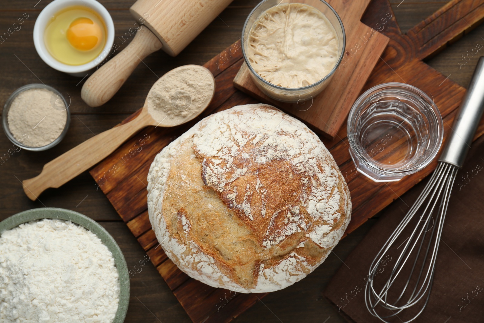 Photo of Freshly baked sourdough bread and ingredients on wooden table, flat lay
