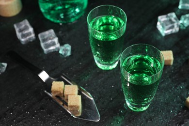 Absinthe in shot glasses, spoon, brown sugar and ice cubes on gray table, closeup. Alcoholic drink