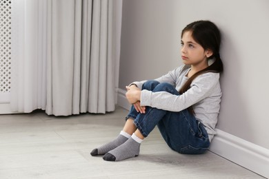 Photo of Sad little girl sitting on floor indoors, space for text