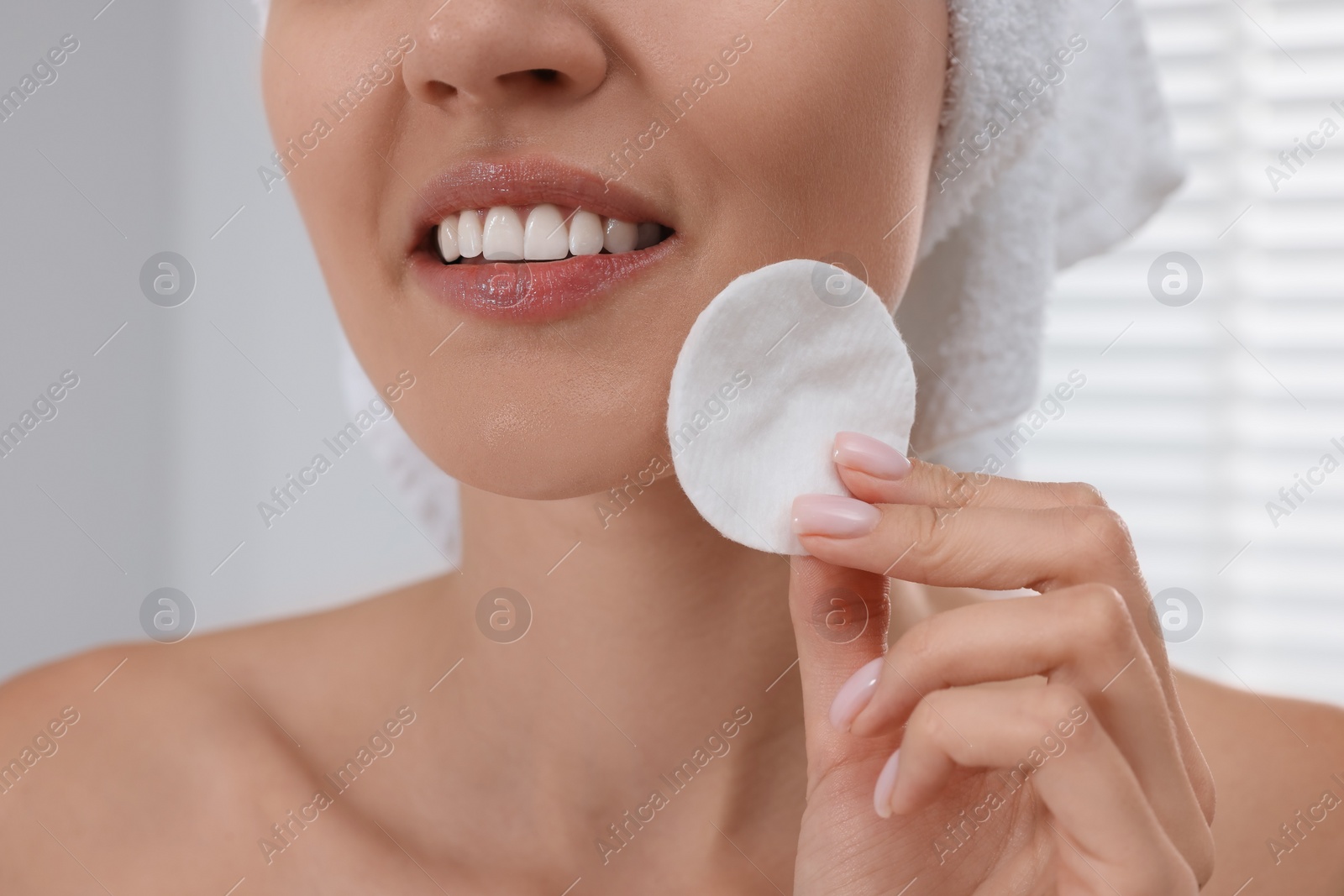 Photo of Young woman cleaning her face with cotton pad indoors, closeup