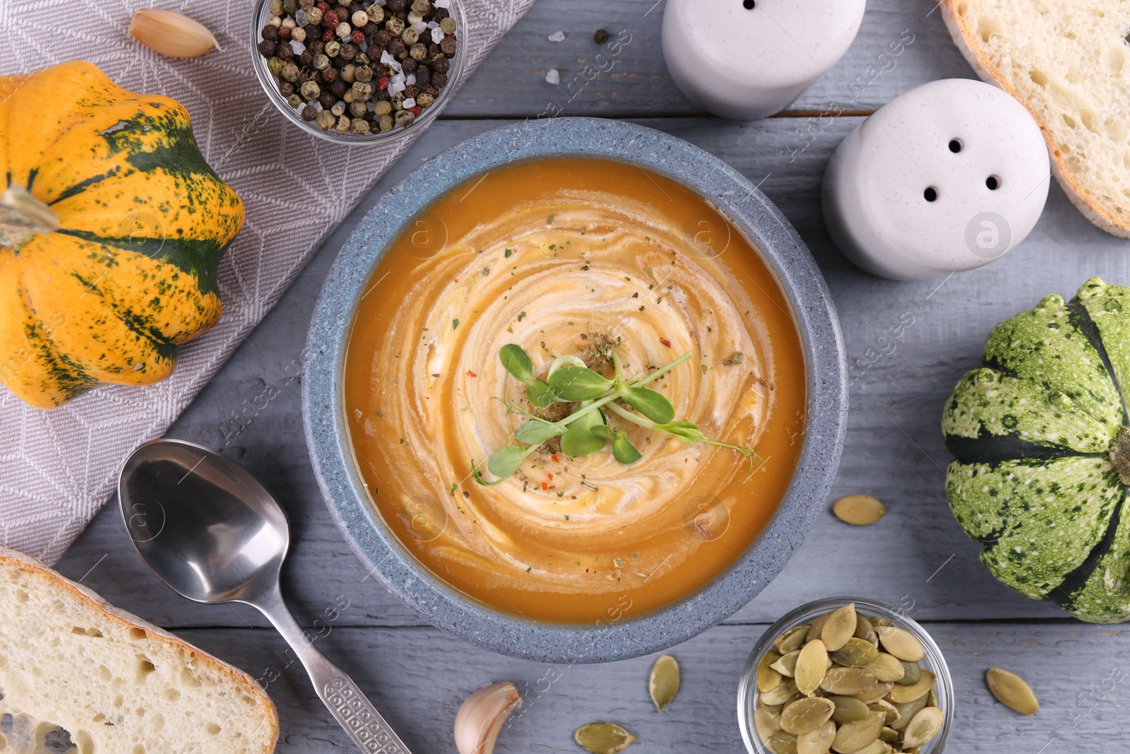 Photo of Flat lay composition with bowl of delicious pumpkin soup on grey wooden table