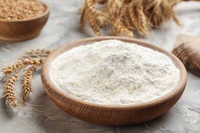 Wooden plate with flour and wheat ears on light grey table, closeup