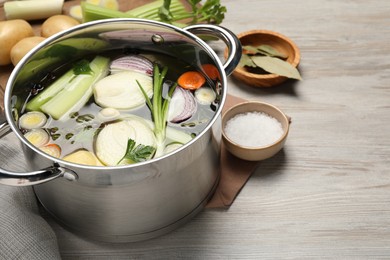 Photo of Pot and different ingredients for cooking tasty bouillon on white wooden table, space for text