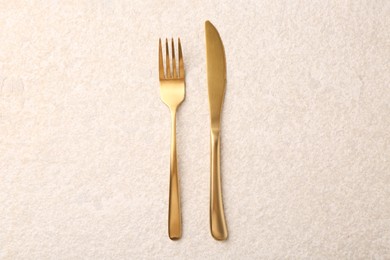 Photo of Elegant cutlery. Golden knife and fork on light textured table, top view