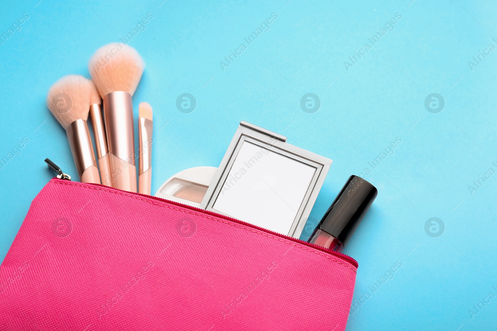Photo of Cosmetic bag with pocket mirror and makeup products on light blue background, flat lay. Space for text