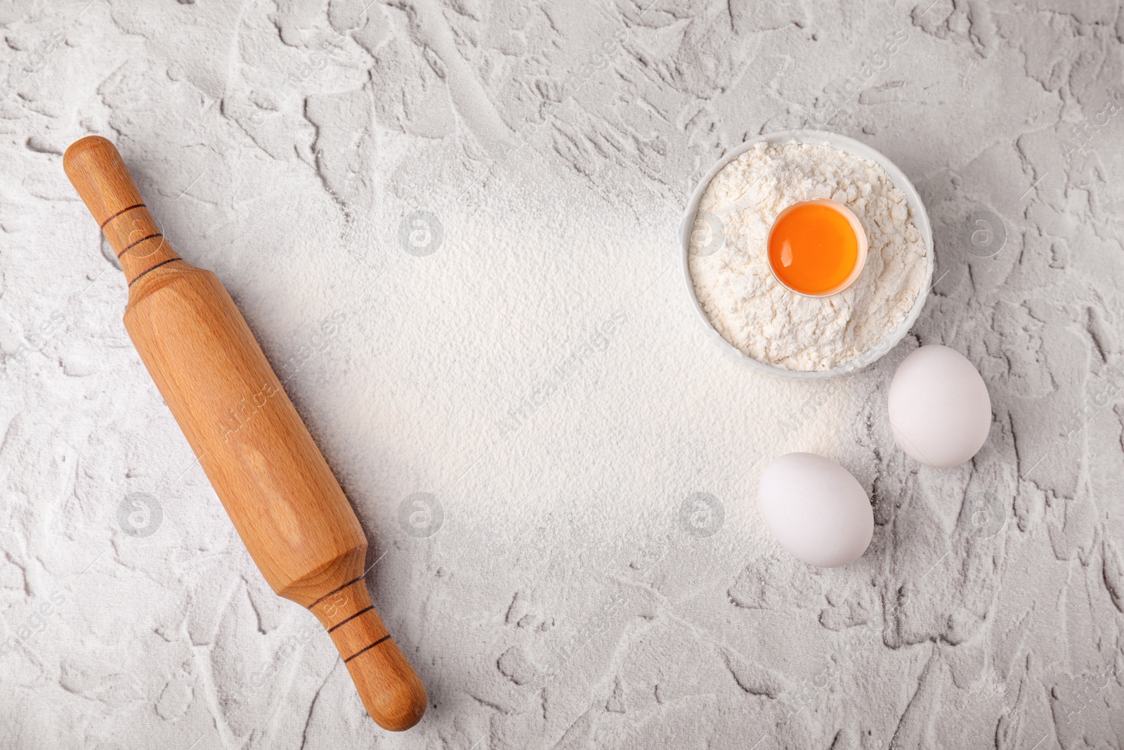 Photo of Flour, rolling pin and eggs on white textured table, flat lay