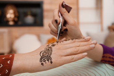 Photo of Professional mehndi master making henna tattoo indoors, closeup