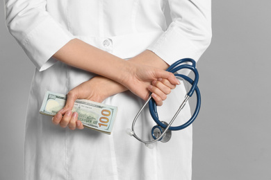 Photo of Doctor with bribe and stethoscope on grey background, closeup. Corruption in medicine