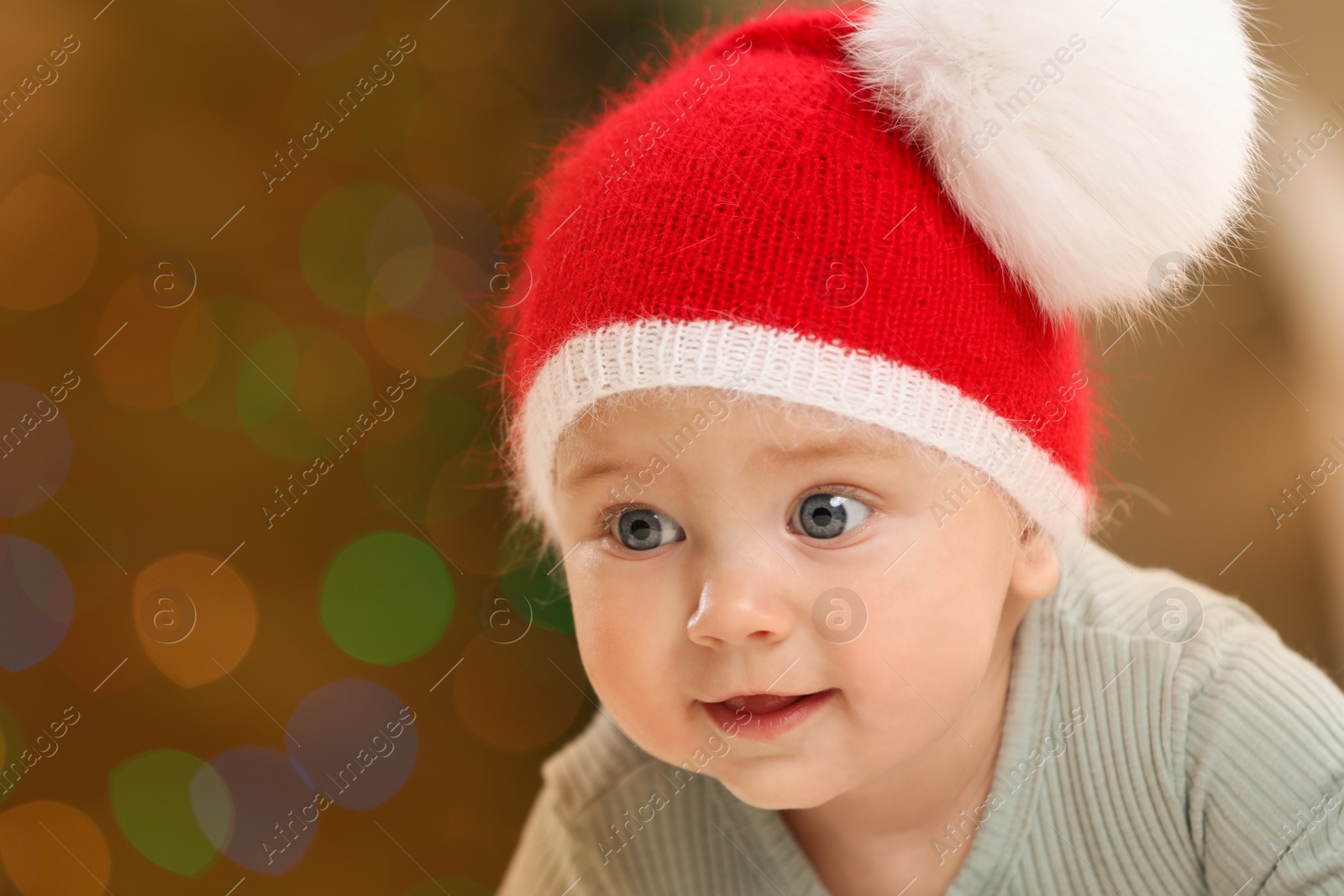 Photo of Cute little baby and blurred Christmas lights on background, space for text. Winter holiday