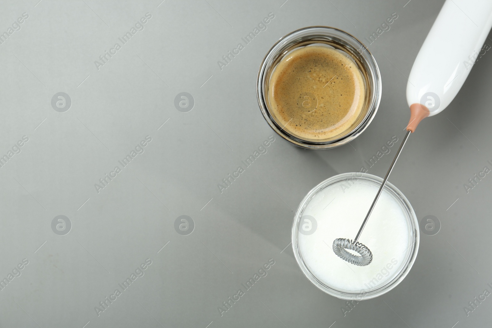 Photo of Mini mixer (milk frother), whipped milk and coffee in glasses on grey background, flat lay. Space for text