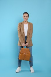 Photo of Beautiful young woman with stylish leather backpack on turquoise background