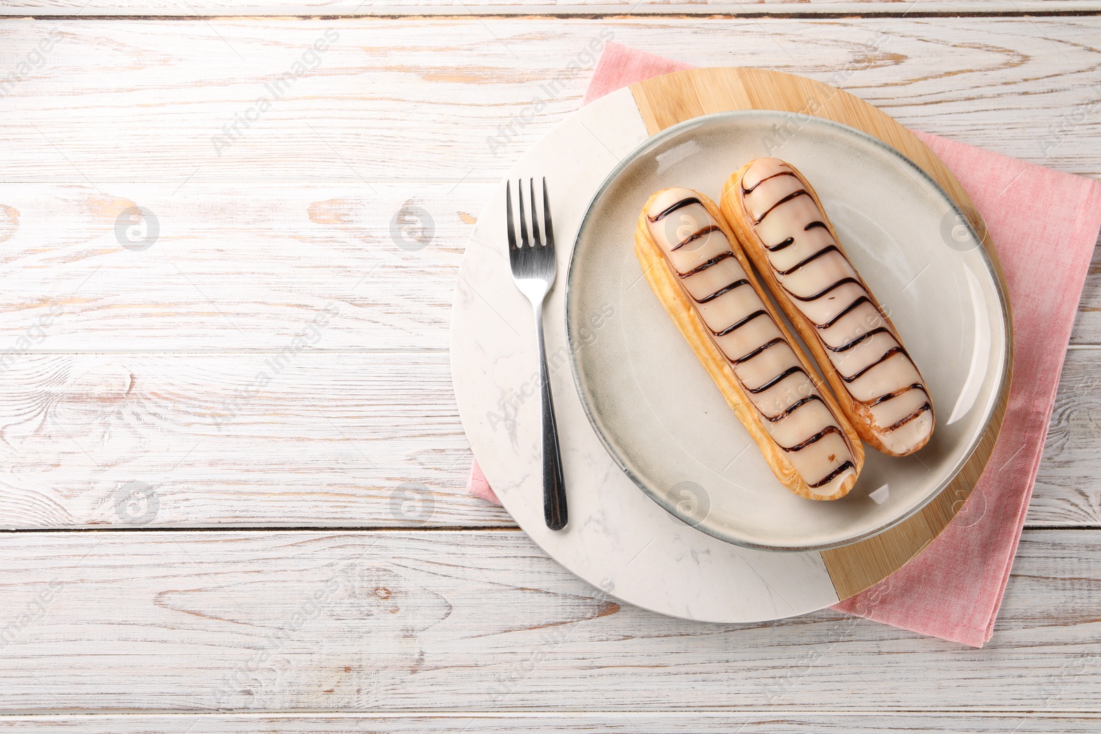 Photo of Tasty glazed eclairs served on wooden rustic table, top view. Space for text