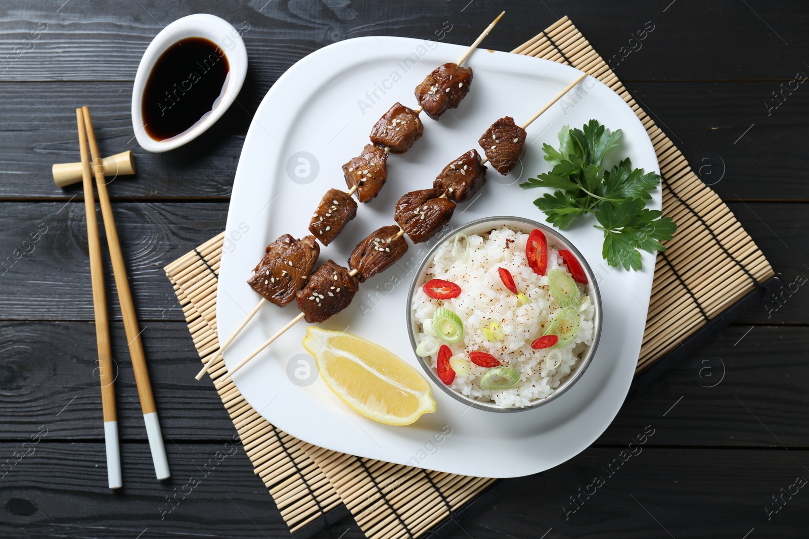 Photo of Tasty chicken meat glazed in soy sauce served with rice on black wooden table, flat lay