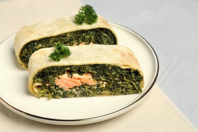 Pieces of delicious strudel with salmon and spinach on light grey table, closeup