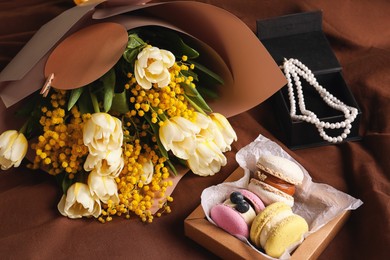 Bouquet of beautiful spring flowers, macarons and necklace on brown fabric