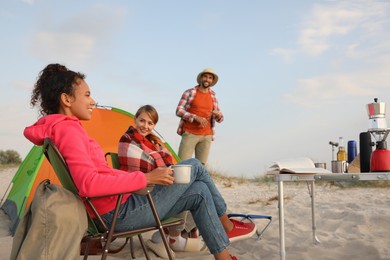 Friends resting near camping tent on sandy beach