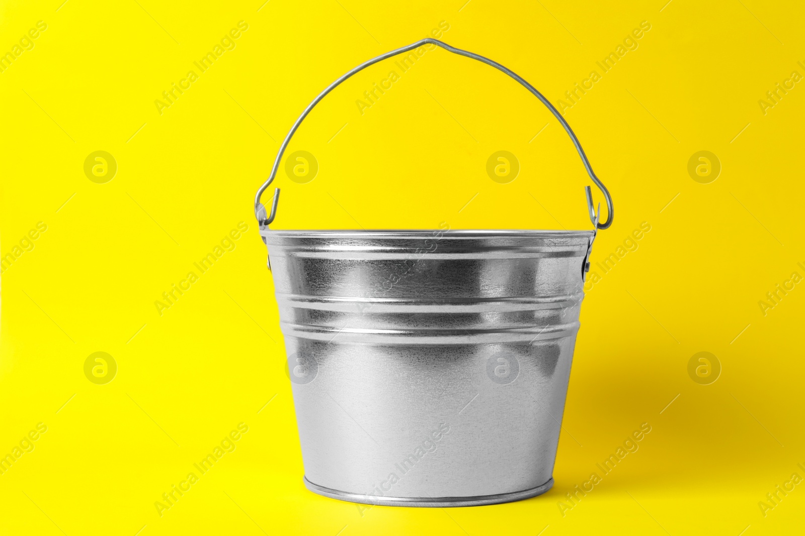 Photo of One shiny metal bucket on yellow background