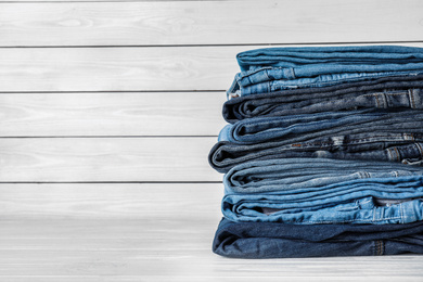 Photo of Stack of different jeans on white wooden table. Space for text