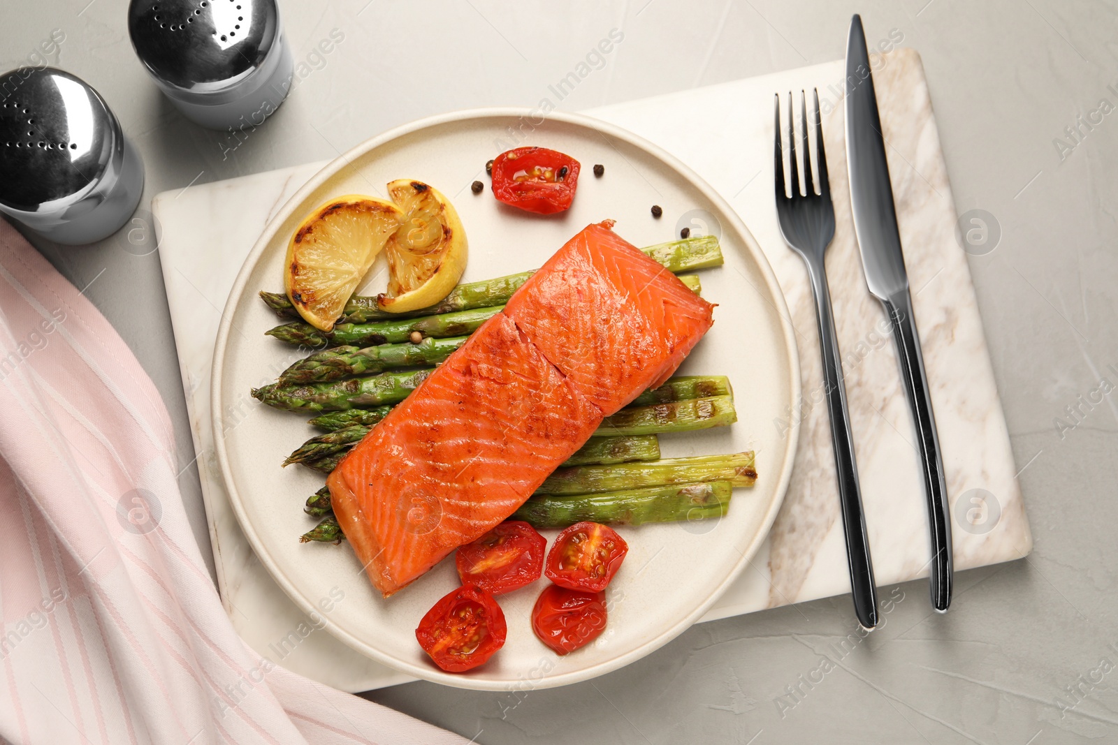 Photo of Tasty grilled salmon with asparagus, tomatoes, spices and lemon served on light grey table, top view