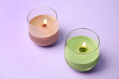 Photo of Burning wax candles in glass holders on purple background