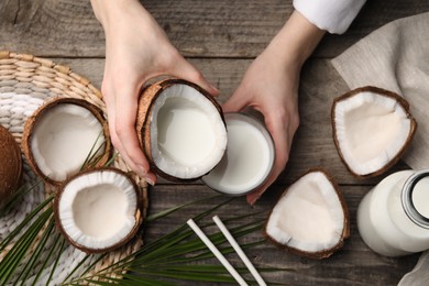 Photo of Woman holding tasty coconut near glass with milk at wooden table, top view