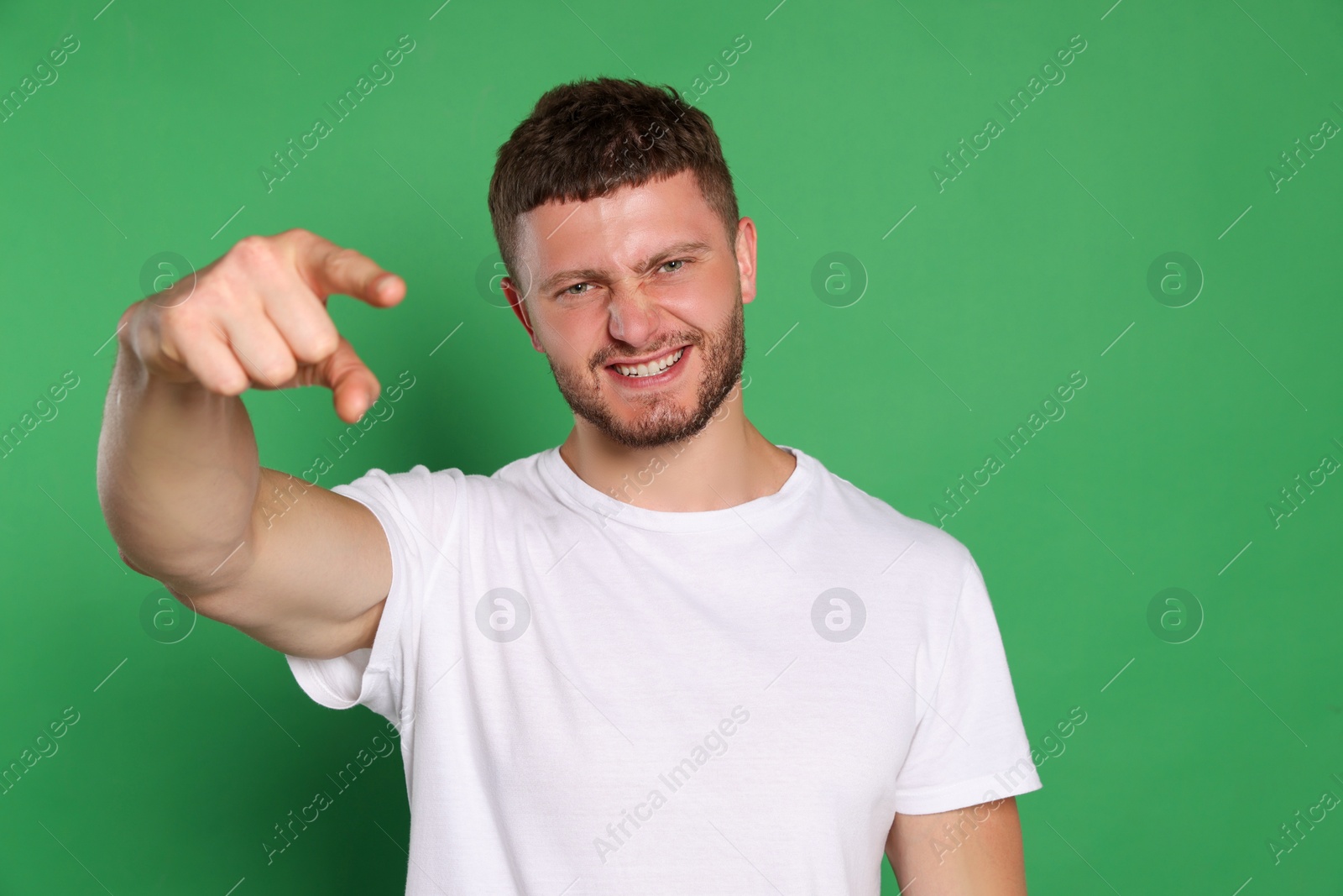 Photo of Aggressive young man pointing on green background