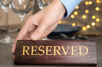 Photo of Waiter setting RESERVED sign on restaurant table, closeup