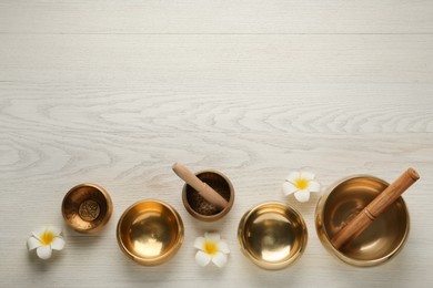 Flat lay composition with golden singing bowls on white wooden table. Space for text
