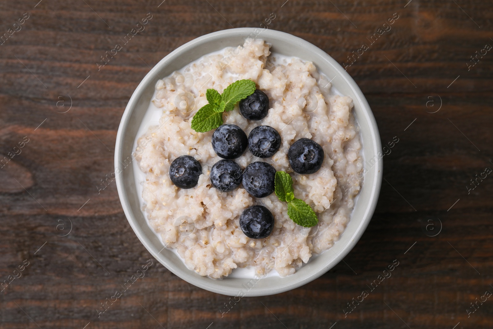 Photo of Delicious barley porridge with blueberries and mint in bowl on wooden table, top view