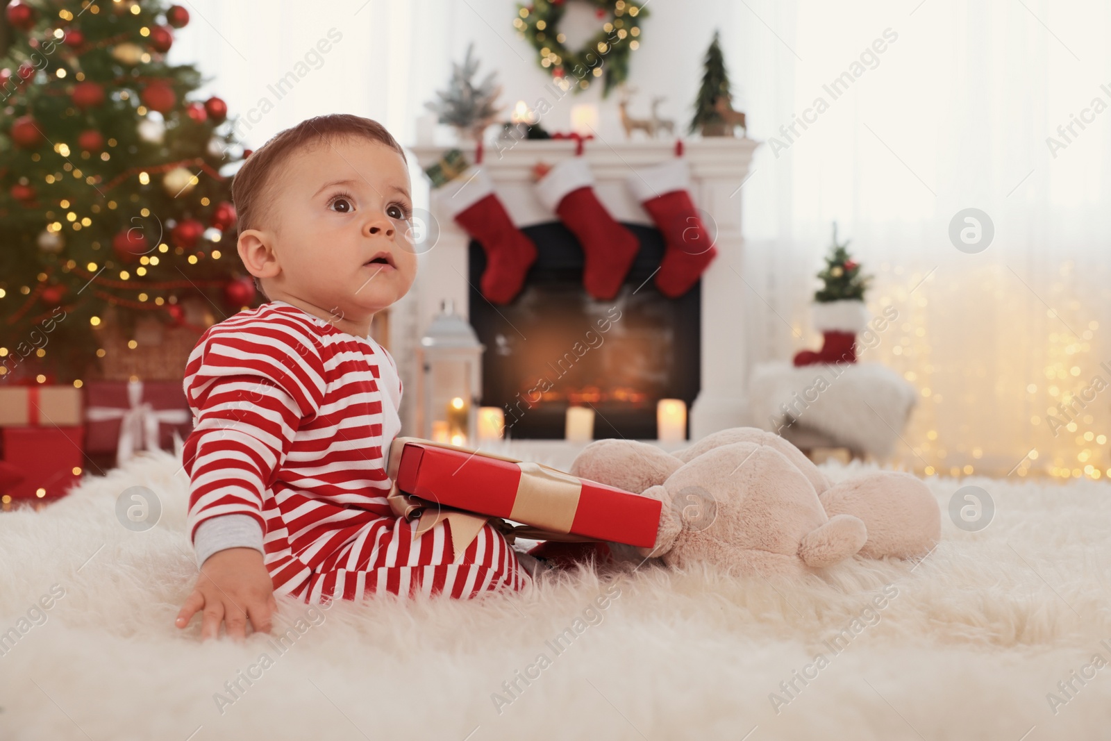 Photo of Cute baby with gift box on floor in room decorated for Christmas