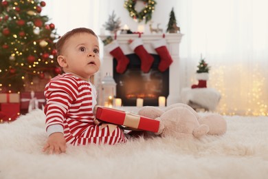 Cute baby with gift box on floor in room decorated for Christmas