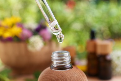 Photo of Dripping essential oil from pipette into bottle on blurred background, closeup