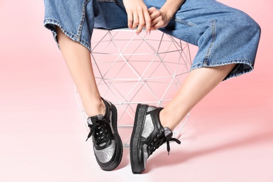 Photo of Woman in stylish shoes on stool against color background, closeup