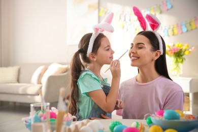 Photo of Happy mother with her cute daughter painting Easter eggs at table indoors