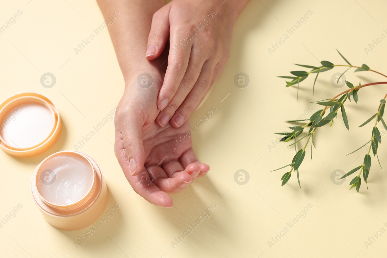 Photo of Woman with jar of hand cream and green twigs on beige background, above view