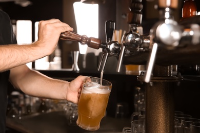 Bartender pouring beer from tap into glass in bar, closeup