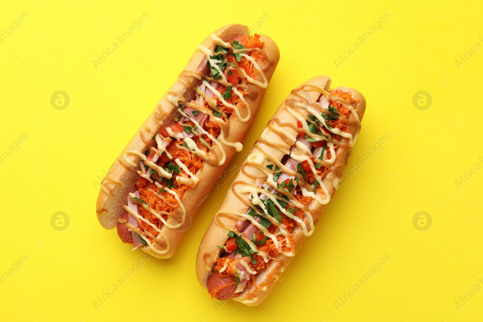 Photo of Delicious hot dogs with bacon, carrot and parsley on yellow background, top view