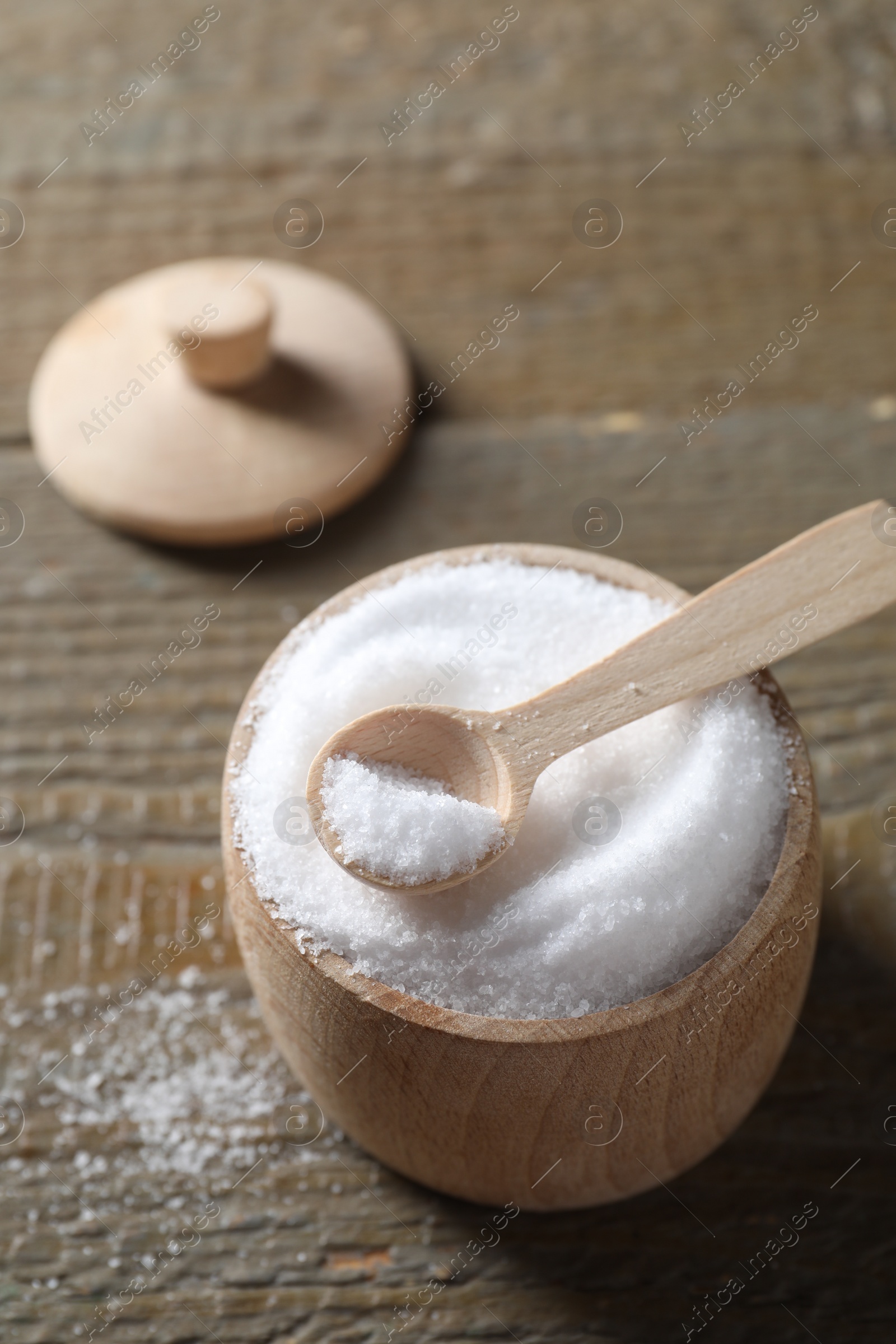 Photo of Organic salt in bowl and spoon on wooden table, closeup