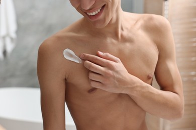 Man applying moisturizing cream onto his shoulder in bathroom, closeup