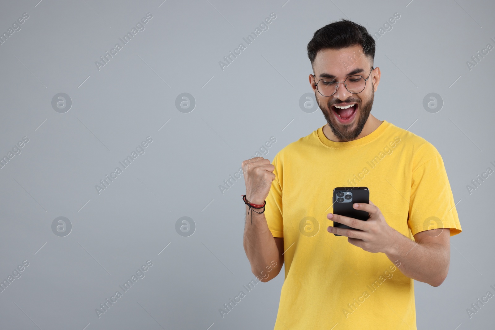 Photo of Happy young man using smartphone on grey background, space for text