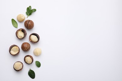 Photo of Tasty Macadamia nuts and green leaves on white background, flat lay. Space for text