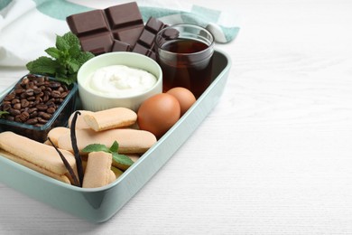 Baking dish with tiramisu ingredients on white wooden table, space for text